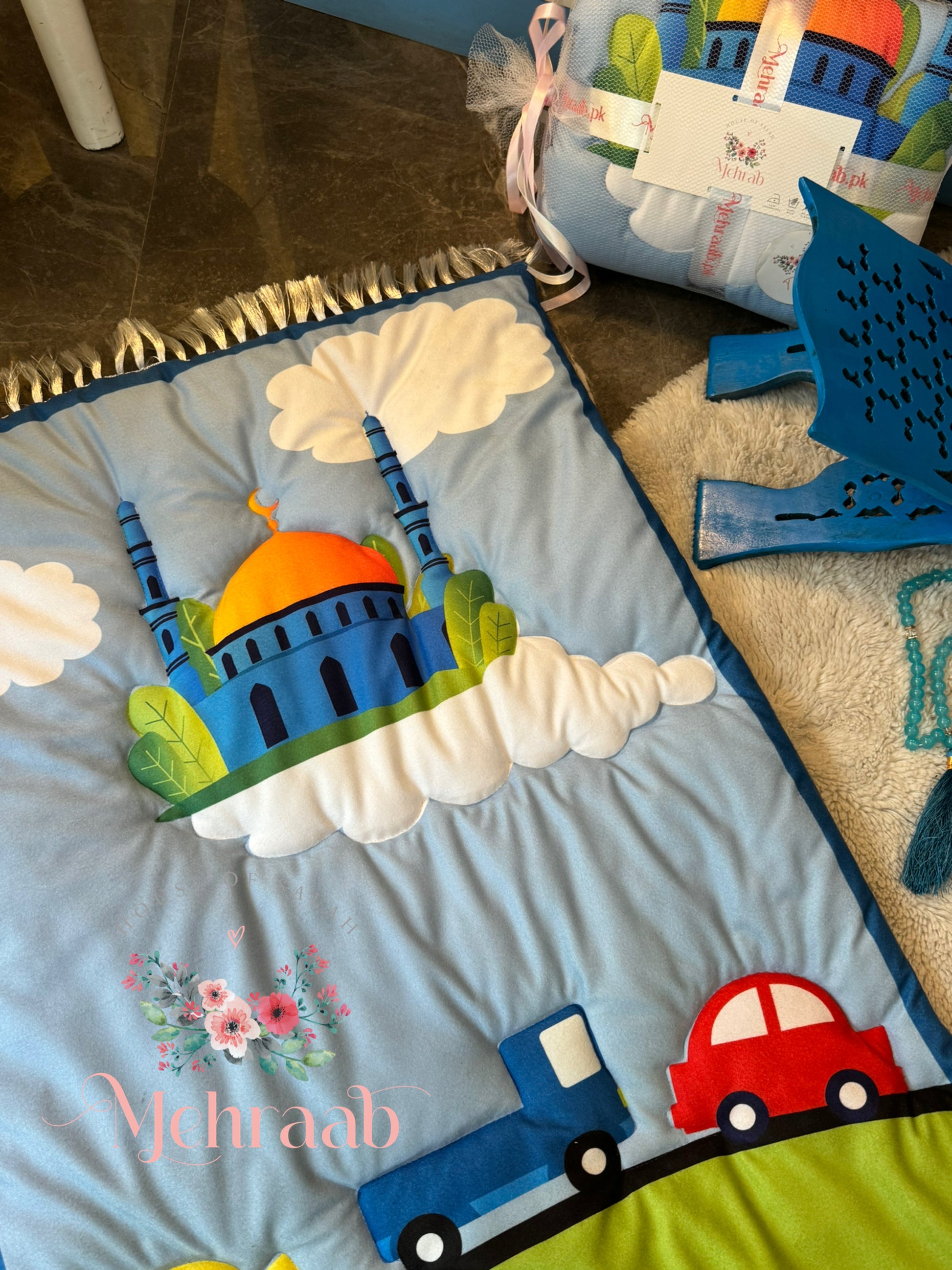 Close up of sky blue janamaz for kids with illustration of mosque and cars